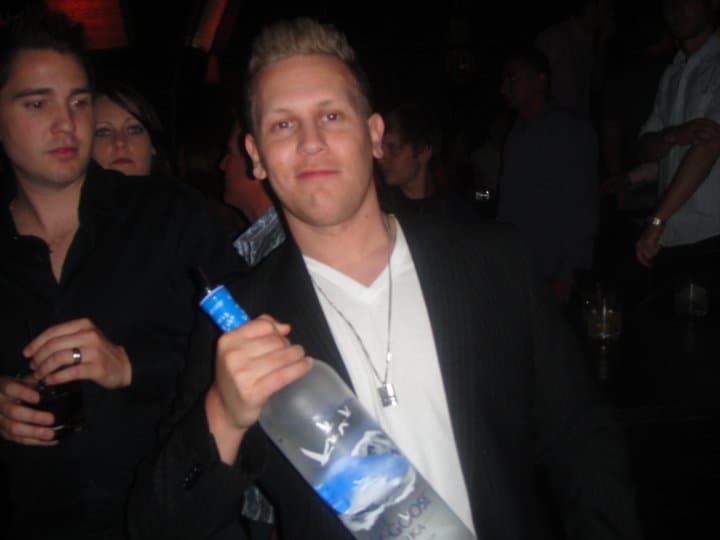 Danny holding a bottle of vodka in a crowded nightclub.