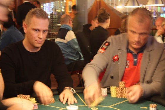 Danny watching the table at a live poker tournament while another player stacks chips.